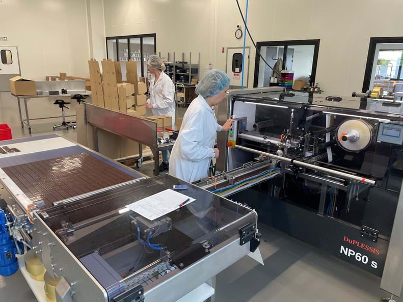 Chocolaterie DuPLESSIS' production factory with two operators wrapping chocolate bars with the Lareka NP60 with buffer belt with dropping station.
